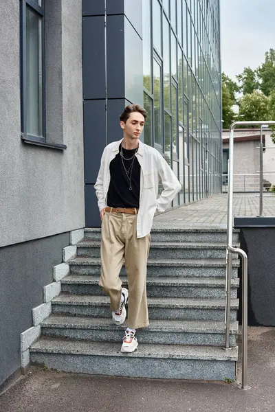 Uma jovem queer pessoa, enfeitada em trajes elegantes, atinge uma pose confiante nos degraus de um edifício. — Fotografia de Stock