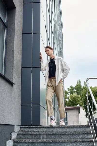 A young queer person in stylish attire stands confidently on the steps of a building celebrating LGBT pride. — Stock Photo