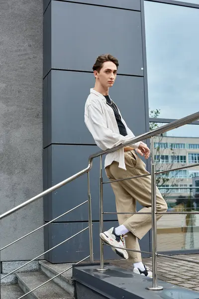 A young queer person in fashionable attire leans thoughtfully on a buildings railing, exuding pride and confidence. — Stock Photo