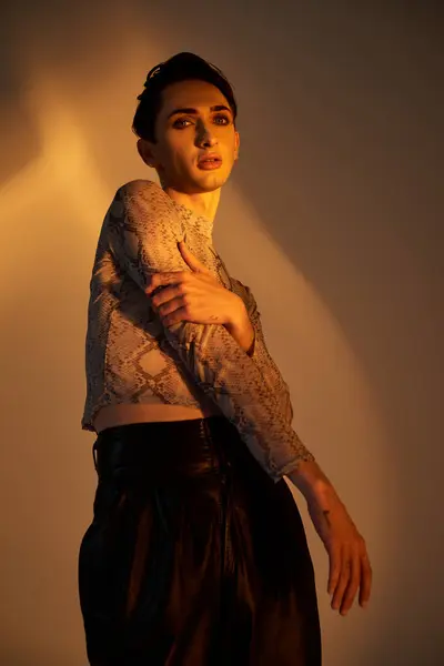 Eine junge queere Person in schwarzer Lederhose posiert selbstbewusst vor einem leuchtenden Licht. — Stockfoto