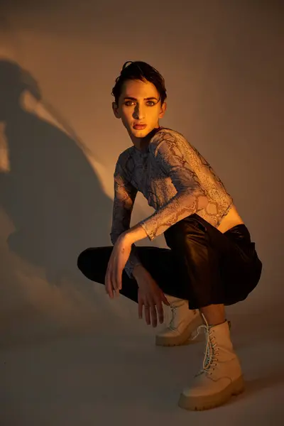 Una joven queer se agacha con un atuendo elegante sobre un fondo blanco, encarnando el orgullo. - foto de stock