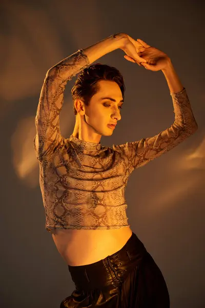 Una persona queer joven con estilo con una parte superior de piel de serpiente y pantalones negros. - foto de stock