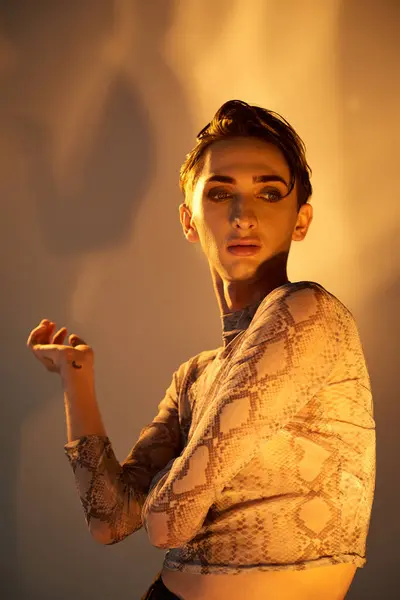 A young queer person in a snakeskin top strikes a pose in front of a bright light, exuding style and confidence. — Stock Photo