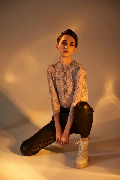 Una persona joven queer, vestida con un atuendo elegante, se agacha en contemplación ante una luz radiante, encarnando el orgullo y el auto-descubrimiento. - foto de stock