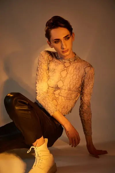 A young queer person strikes a confident pose in a top and leather pants, exuding style and pride in front of a white background. — Stock Photo