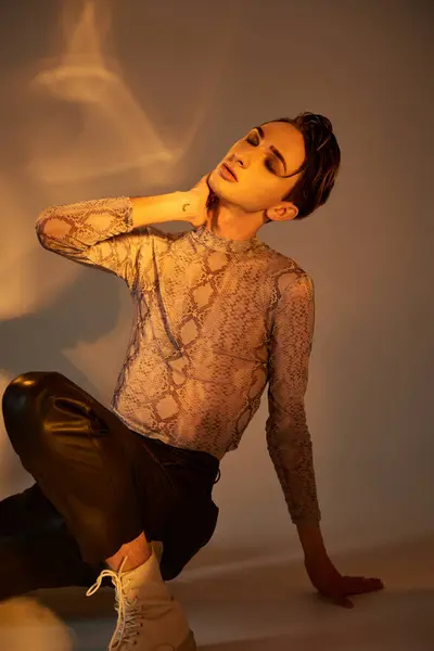 A stylish, confident young queer person strikes a pose in front of a radiant light, embodying pride and self-expression. — Stock Photo