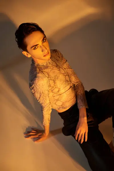 A young queer person in stylish black pants poses on the floor exuding confidence and pride. — Stock Photo