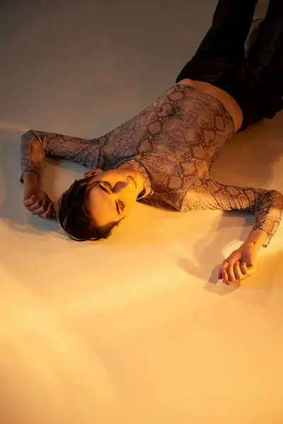 Young queer person in stylish attire lays on floor, bathed in light, exuding confidence and pride. — Stock Photo