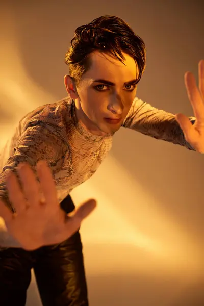 A stylish young queer person with outstretched hands in front of a radiant light, embodying pride and acceptance. — Stock Photo