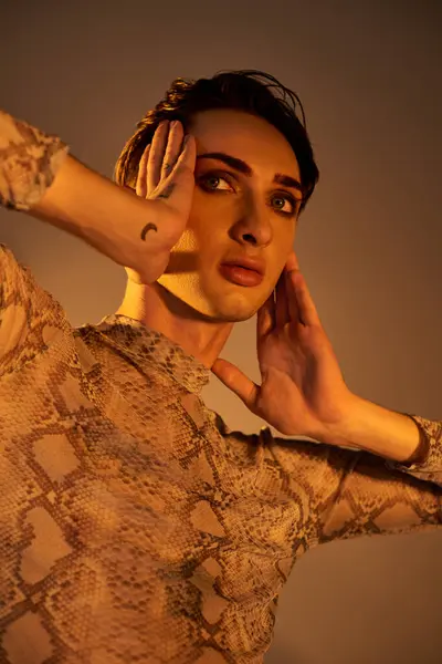 A young queer in a snake skin dress poses with hands on her ears in a stylish, pride-inspired ensemble. — Stock Photo