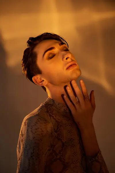 Un giovane uomo queer, vestito con stile, colpisce una posa pensosa con mano sul mento, incarnando sia orgoglio che introspezione.. — Foto stock
