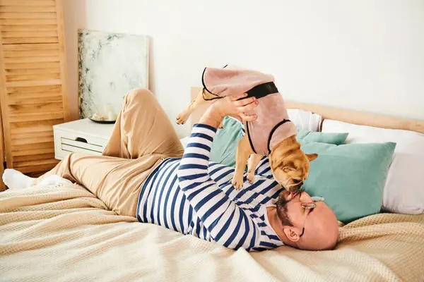 Bello uomo coccole con piccolo Bulldog francese sul letto. — Foto stock