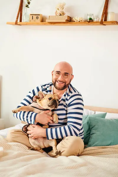 A man with glasses sitting on a bed cuddling with two French bulldogs. — Stock Photo