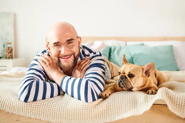 Schöner Mann mit Brille entspannt auf dem Bett neben seiner treuen französischen Bulldogge. — Stockfoto