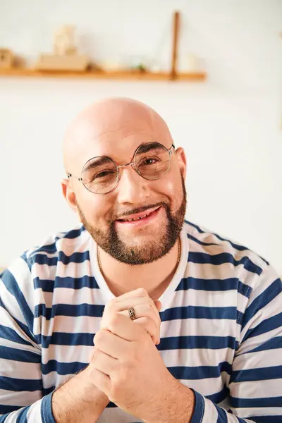 A bald man in glasses strikes a thoughtful pose at home. — Stock Photo