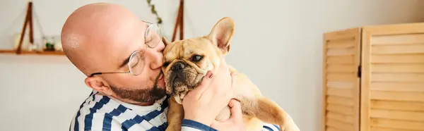 A man with glasses holds a small French bulldog in his arms. — Stock Photo