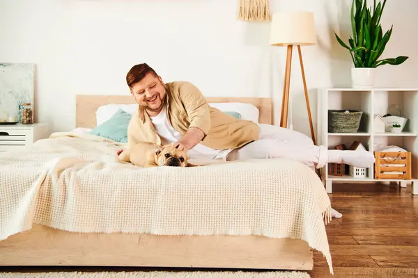 Ein schöner Mann entspannt sich auf einem Bett mit seiner Französischen Bulldogge. — Stockfoto