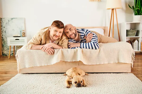 Two men, together with their French bulldog, relax on a bed in a cozy setting. — Stock Photo