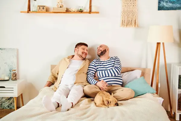 A gay couple lounges on a bed with their French bulldog nearby. — Stock Photo
