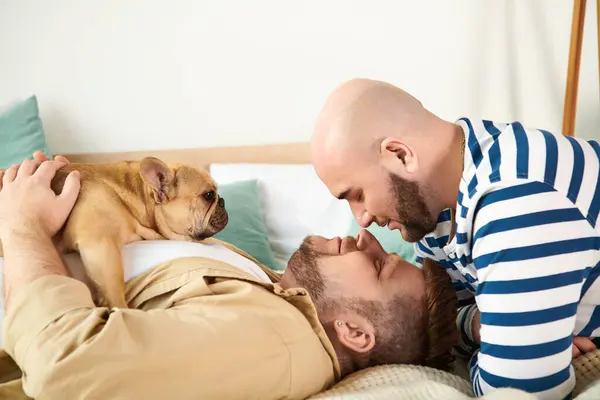 Dos hombres y un perro descansan tranquilamente juntos en una cama. - foto de stock