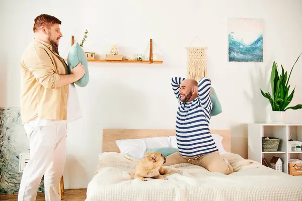 Two men standing together on a bed next to a French bulldog. — Stock Photo