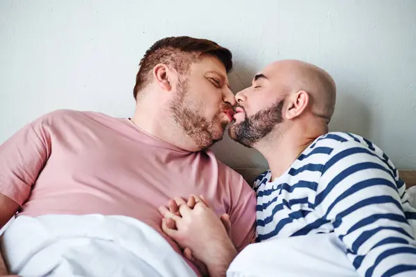 Un par de hombres acostados en la cama compartiendo un tierno beso. - foto de stock