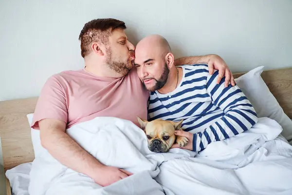Two men relax in bed, cuddling with their French bulldog. — Stock Photo