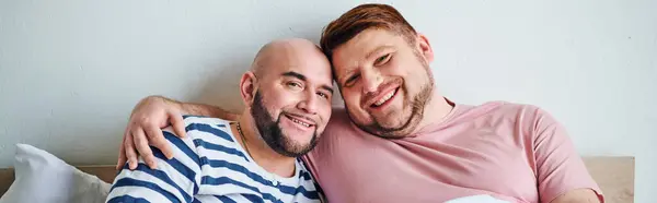 Una pareja gay sentados juntos en una cama. - foto de stock