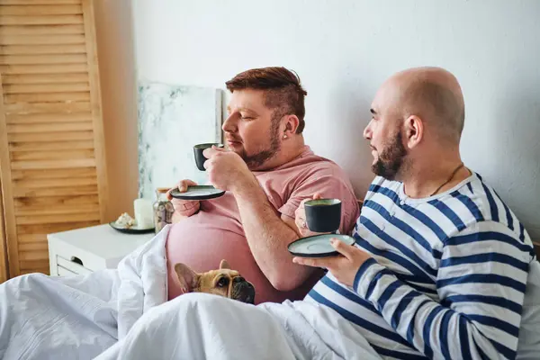 A gay couple and their French Bulldog lounging on a bed. — Stock Photo