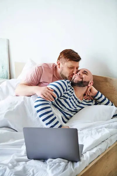 Due uomini coccolati a letto con un computer portatile. — Foto stock