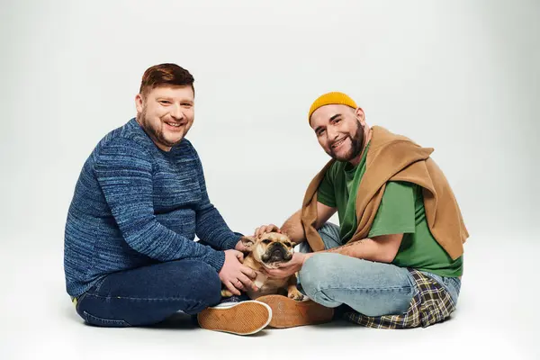 Una pareja gay amorosa sentada junto con su amado Bulldog francés. - foto de stock