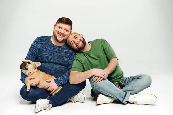 Una pareja gay amorosa sentados juntos, sosteniendo un lindo Bulldog francés. - foto de stock