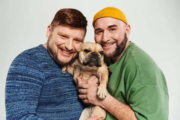 Una pareja gay amorosa sosteniendo a su pequeño Bulldog francés con cuidado y afecto. - foto de stock