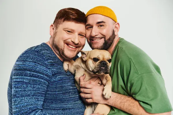 Dos hombres se abrazan tiernamente, sosteniendo un perro pequeño juntos. - foto de stock