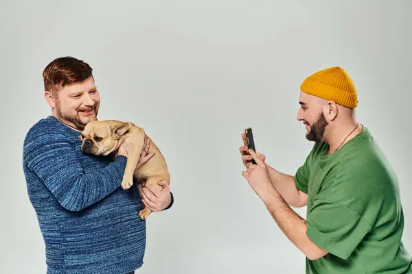 Zwei Männer stehen eng beieinander und halten eine französische Bulldogge in der Hand. — Stockfoto
