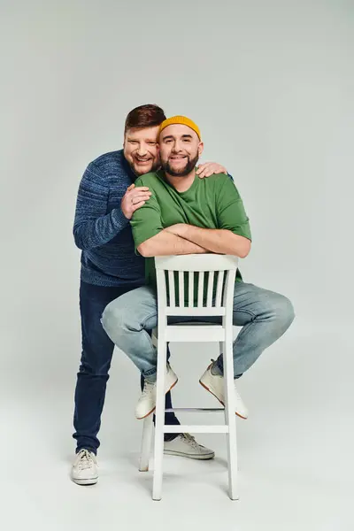 Двоє чоловіків обіймаються ласкаво на стільці, демонструючи любов і спокій в інтимний момент. — стокове фото