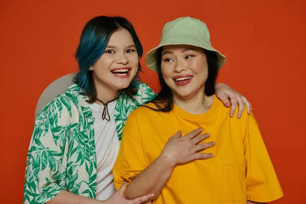 Una madre asiática y su hija adolescente posan elegantemente para una foto en un estudio sobre un fondo naranja. - foto de stock