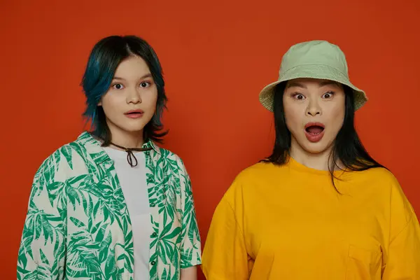 Asian mother and her teenage daughter standing next to each other in a studio against an orange background. — Stock Photo