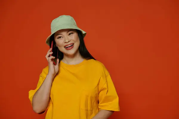 Une femme en chemise jaune parle sur un téléphone portable sur un fond orange. — Photo de stock