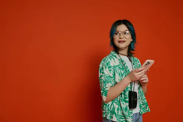 Uma menina adolescente elegante com cabelo azul e óculos mantém um telefone celular em um estúdio vibrante. — Fotografia de Stock