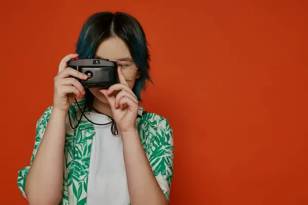 Ásia teen menina segura um câmera até ela rosto no um estúdio no um laranja fundo. — Fotografia de Stock