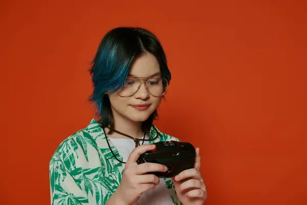 Ein Teenie-Mädchen mit leuchtend blauen Haaren in einem Studio-Setting mit einer Kamera vor orangefarbenem Hintergrund. — Stockfoto