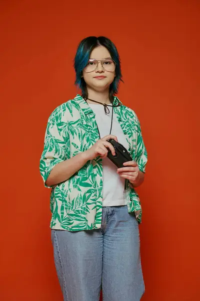 A girl stands before a red wall, holding a camera confidently. — Stock Photo