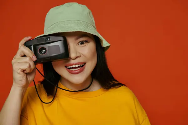A woman holding a camera up to her face in a studio on an orange background. — Stock Photo