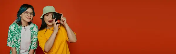 Asian mother and her teenage daughter standing side by side, both holding camera on an orange background. — Stock Photo