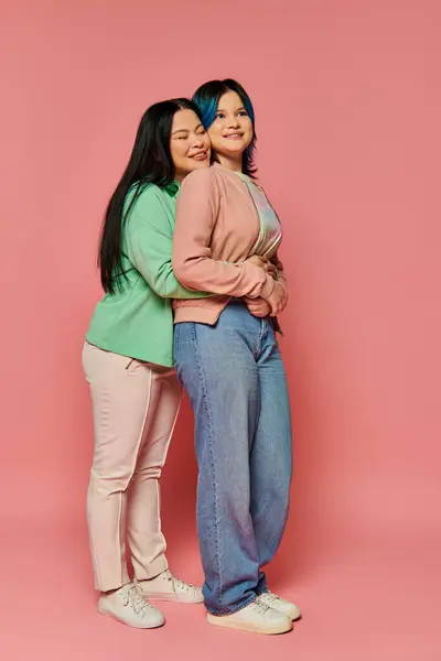 Asiatische Mutter und Teenagertochter in lässiger Kleidung stehen gemeinsam vor einem leuchtend rosa Hintergrund und strahlen Verbundenheit und Einheit aus. — Stockfoto