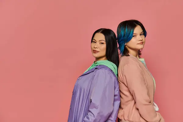 Uma mãe asiática elegante e sua filha adolescente, ambos com cabelo azul vibrante, posar juntos em um fundo de estúdio rosa. — Fotografia de Stock