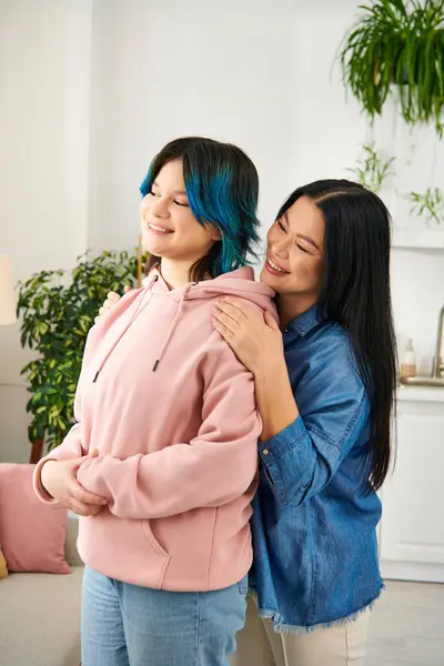 An Asian mother and her teenage daughter stand side by side in a cozy living room, sharing a moment of connection and warmth. — Stock Photo