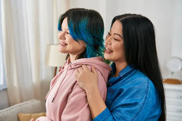 Une mère asiatique et sa fille adolescente aux cheveux bleus s'embrassant chaleureusement à la maison, affichant amour et connexion. — Photo de stock