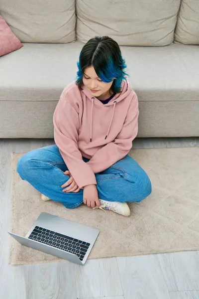 Дівчина з блакитним волоссям сидить поруч з ноутбуком на підлозі, глибоко в думці — стокове фото
